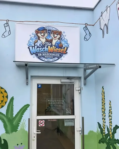 Eingang des Waschsalons: Glastür in einer hellblau bemalten Wand, darüber das Schild mit dem WaschWiesel-Logo
